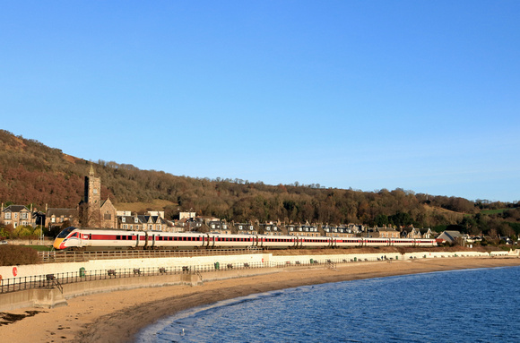 LNER Azuma Class 800 No 800107 skirts along the beach overlooking the  the Firth of Forth at Burntisland, Fife on 6.12.23 with 1W02 0708 Leeds to Aberdeen service passing Erskine Church